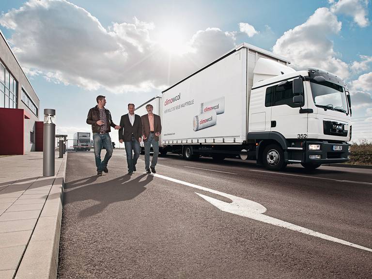 Drei Mitarbeiter stehen auf dem Firmengelände vor einem LKW